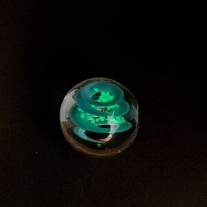 May include: A clear glass paperweight with a swirling green design inside. The design is reminiscent of a spiral or a vortex.