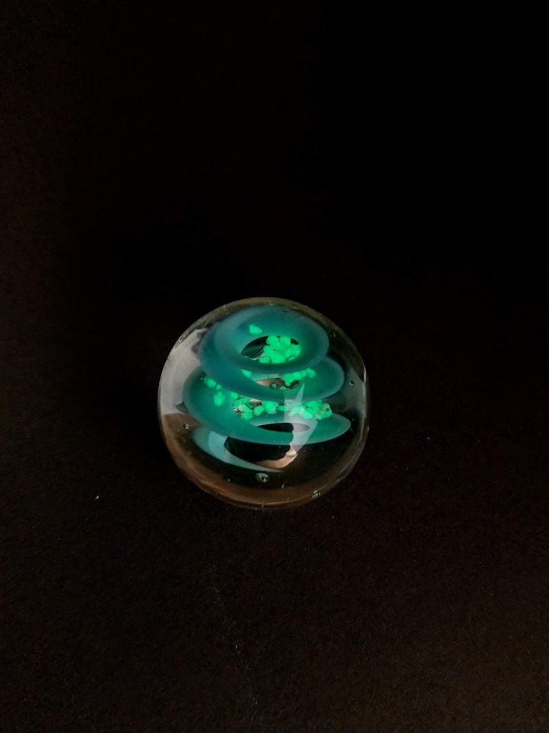 May include: A clear glass paperweight with a swirling green design inside. The design is reminiscent of a spiral or a vortex.