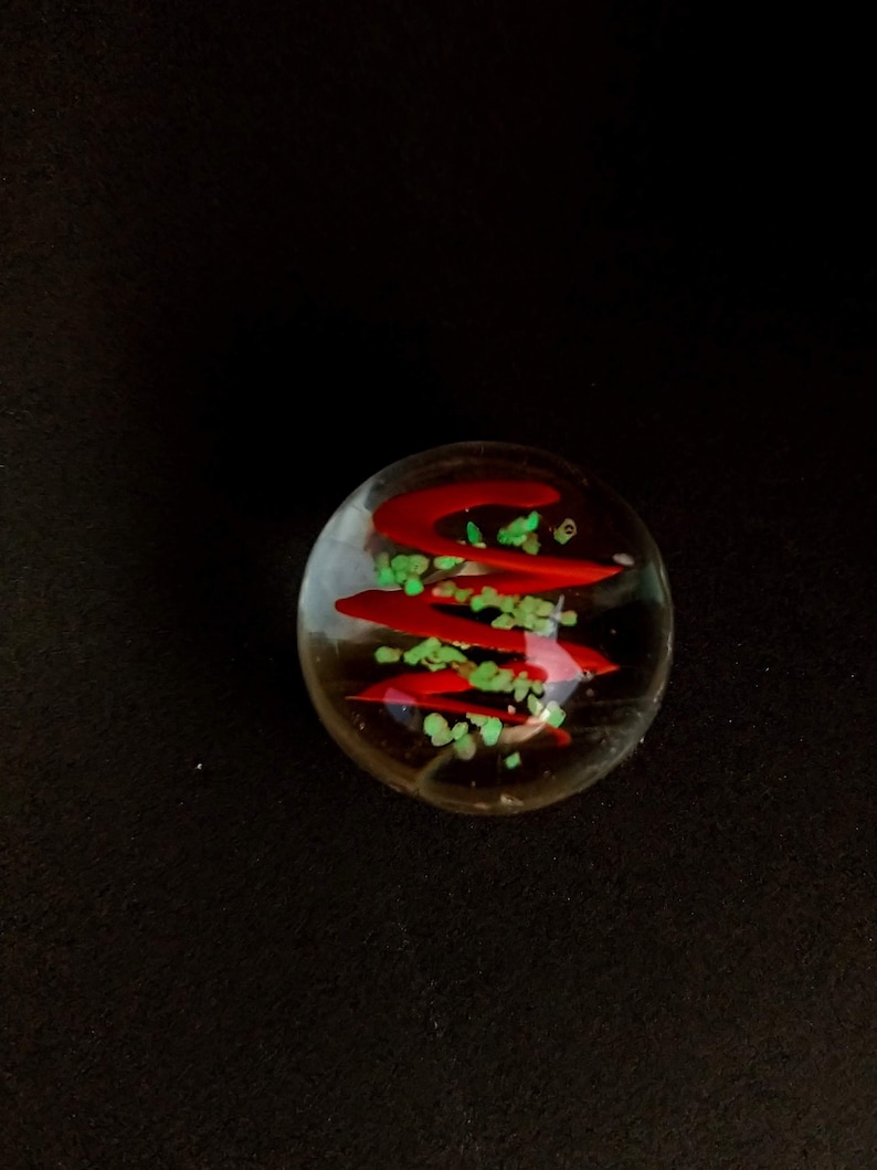 May include: A clear glass marble with red and green swirls inside. The marble has a shiny finish.