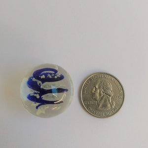 May include: A clear glass marble with blue and white swirls inside. The marble is about the size of a US quarter.