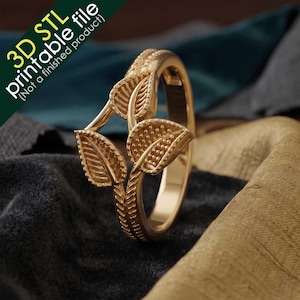 Puede incluir: Un anillo de color dorado que presenta tres elementos en forma de hoja con superficies texturizadas y una banda con patrón de espiga. La imagen incluye el texto 3D STL printable file (Not a finished product) en la esquina superior izquierda.