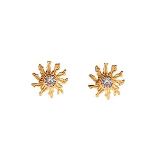 May include: A pair of gold earrings with a sunburst design and a small clear rhinestone in the center of each earring.