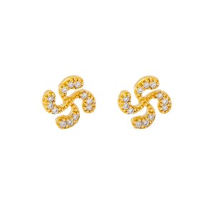 May include: A pair of gold-colored stud earrings. Each earring features a swirling, four-petal design, encrusted with small, clear gemstones. The earrings are set against a plain white background.