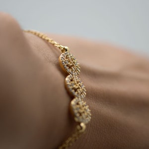 May include: A gold bracelet with a delicate chain and multiple round charms encrusted with small clear stones.