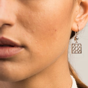 Può includere: Orecchini pendenti in argento con un design geometrico quadrato. Gli orecchini hanno una piccola perla rotonda nella parte superiore del pendente.