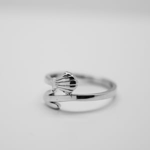May include: A silver ring with a seashell design. The ring is open and adjustable.