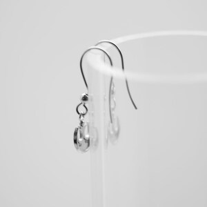 May include: A pair of silver earrings with a simple design hanging from a clear glass container.