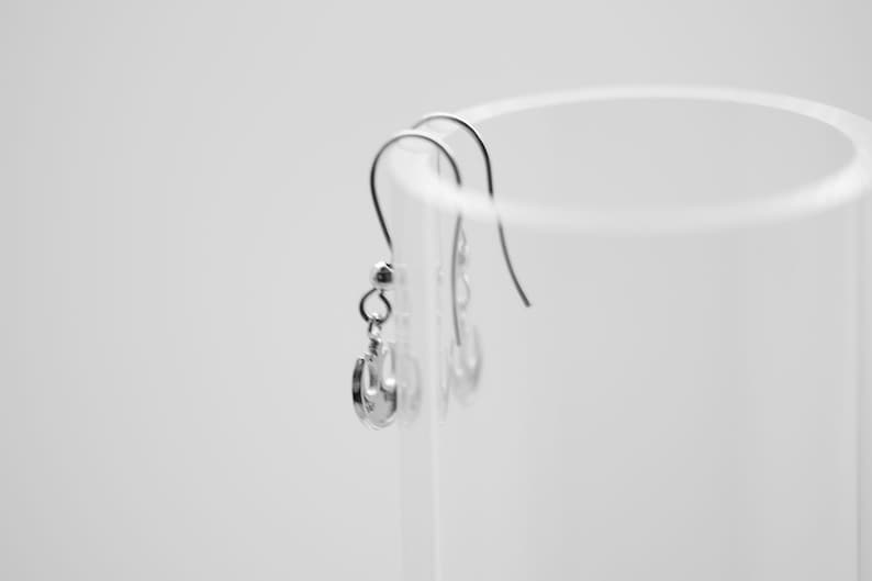 May include: A pair of silver earrings with a simple design hanging from a clear glass container.