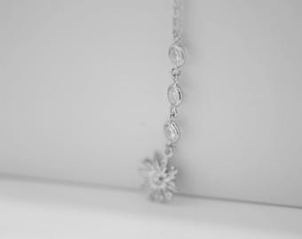 May include: A silver chain necklace with a flower-shaped pendant made of small, clear stones.