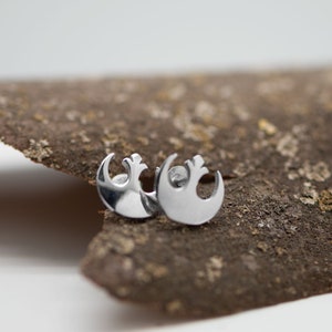 May include: A pair of silver Rebel Alliance symbol earrings. The earrings are small and delicate, and they are perfect for any Star Wars fan.