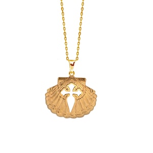 Op de afbeelding: Een gouden ketting met een hanger in de vorm van een schelp met een uitgeknipt kruis in het midden.