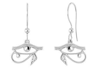 Puede incluir: Un par de pendientes colgantes de tono plateado con el símbolo del Ojo de Horus. Cada pendiente consta de un dije de metal pulido suspendido de un gancho simple con una pequeña cuenta esférica, mostrando el diseño detallado del ojo.