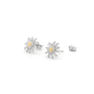 Puede incluir: Un par de pendientes de plata con diseño floral. Cada pendiente presenta un contorno detallado y puntiagudo con un centro dorado. También se ve un cierre de pendiente, sobre un fondo blanco.