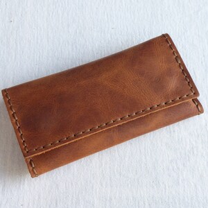 May include: A brown leather key holder with a stitched edge.