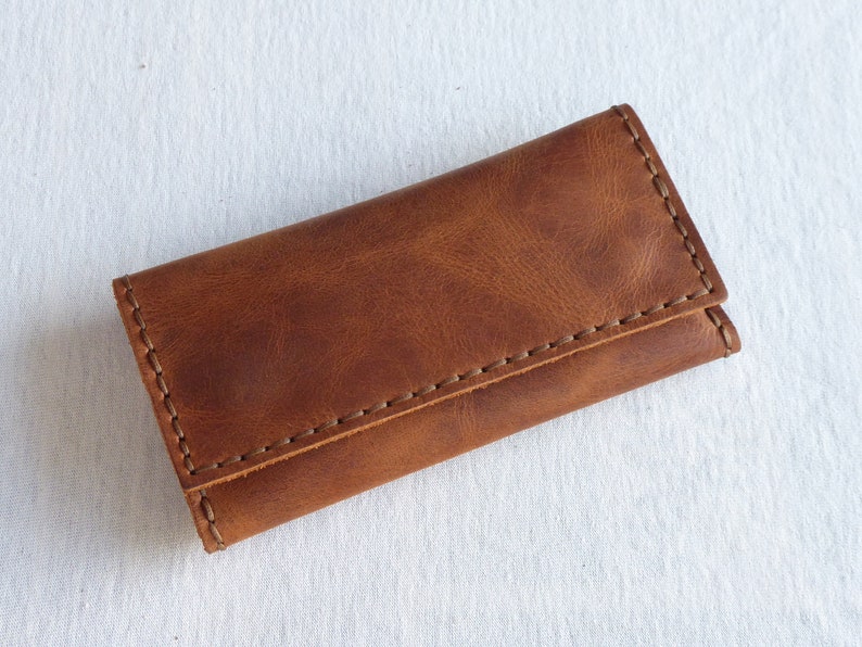 May include: A brown leather key holder with a stitched edge.