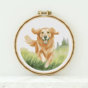 Puede incluir: Un patrón de punto de cruz de un golden retriever corriendo por un campo de hierba verde. El perro está sonriendo y tiene la lengua fuera. El fondo es una acuarela de verde y azul.