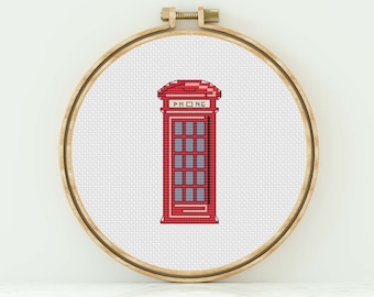 May include: Red telephone booth cross-stitch pattern in a wooden embroidery hoop. The booth has a white sign that says "PHONE".
