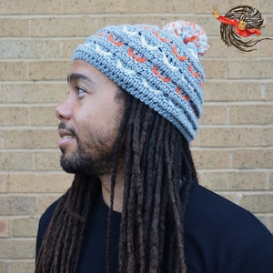 May include: A man with long dreadlocks is wearing a gray and orange crocheted beanie with a white pom pom on top.