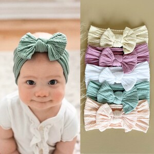 May include: Set of six knotted headbands in various colours, including cream, pink, white, and green. The headbands are made of a soft, stretchy fabric and have a knotted bow detail.