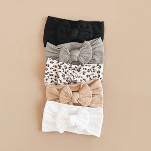May include: Four different fabric headbands with knotted bows. The headbands are in black, grey, brown with a leopard print, and white.