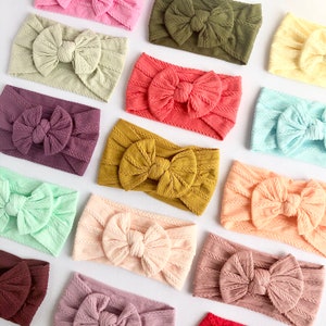 May include: A collection of 12 different coloured knotted headbands with a textured fabric. The headbands are arranged in a semi-circle on a white background.