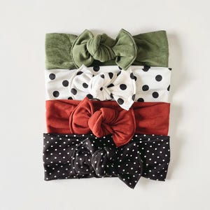May include: Set of four knotted headbands in various colours and patterns. The headbands are made of soft fabric and feature a variety of polka dot designs. The set includes a green headband, a white headband with black polka dots, a red headband, and a black headband with white polka dots.