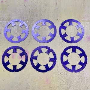 Puede incluir: Seis objetos circulares de metal púrpura con un diseño de estrella. Cada objeto tiene un agujero central y está rodeado de formas recortadas. Los objetos están dispuestos en dos filas de tres.