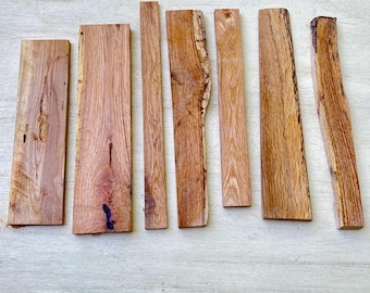 May include: A collection of seven rectangular wooden planks with varying widths and lengths. The planks display natural wood grain patterns and warm brown tones, with some featuring the original bark edge. The wood appears to be unfinished.