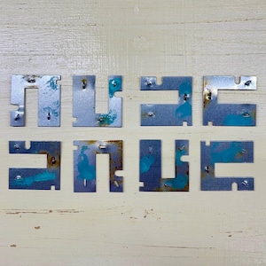 May include: Eight metal pieces spelling out the word "MUSIC" and "SAVE". The metal has a silver finish with areas of rust and turquoise paint. The pieces are arranged on a light wood surface.