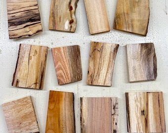 May include: A collection of twelve rectangular wooden coasters with natural edges. The coasters display a variety of wood grain patterns and colors, ranging from light beige to dark brown. Each coaster is approximately 4 inches long and 3 inches wide.