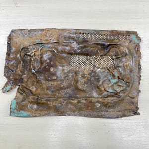 Peut inclure: Une plaque de métal rectangulaire vieillie avec une section perforée. Le métal présente une surface corrodée texturée avec des nuances de marron, de cuivre et des touches de turquoise. Les bords sont inégaux, suggérant l'âge et l'usure.