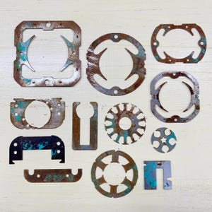 May include: A collection of irregularly shaped, rusty metal pieces with various cut-out designs. Some pieces have patches of teal-colored paint. The shapes include circles, squares, and other geometric forms, all with a weathered appearance.