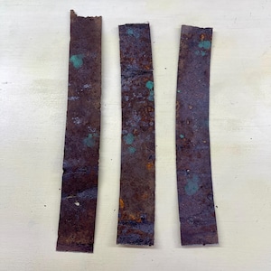 Peut inclure: Trois bandes rectangulaires de métal vieilli, présentant une riche teinte brun rouille avec des taches d'oxydation vert-turquoise. Les bandes sont disposées verticalement, mettant en valeur leur texture vieillie et leurs variations de couleurs uniques.