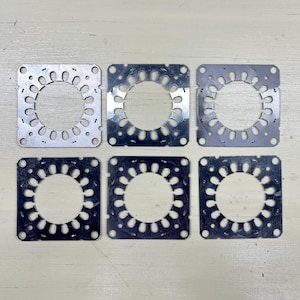 May include: Six square metal plates with a central circular opening and a pattern of smaller holes and curved cutouts around the perimeter. The plates are arranged in two rows of three on a light-colored surface.