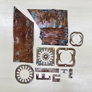 Peut inclure: Diverses pièces en métal de cuivre patiné, comprenant des formes rectangulaires et circulaires, avec des patines marron, orange et turquoise. La collection présente diverses découpes et bords irréguliers, suggérant des matériaux recyclés ou récupérés.