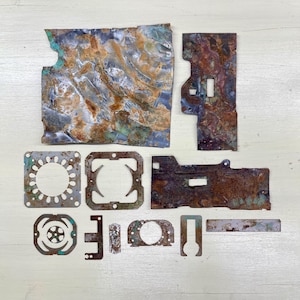 May include: An assortment of weathered metal pieces with a distressed, aged appearance. The pieces vary in shape and size, featuring a mix of rectangular, square, and irregularly shaped components. Colors include shades of brown, rust, and hints of blue and green.