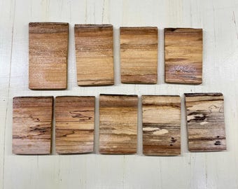 May include: Ten rectangular wooden coasters with a natural wood grain pattern. The coasters are various shades of brown and tan, with unique grain variations. They are arranged on a light-colored surface.