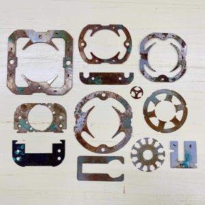 May include: A collection of irregularly shaped, rusted metal pieces with various cut-out designs. The pieces have a mix of brown, blue, and white coloration, suggesting age and exposure to the elements. The shapes include circles, squares, and other geometric forms.