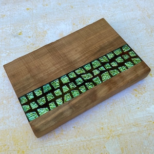 May include: A wooden serving board with a green mosaic inlay. The mosaic is made of small, irregular pieces of glass that are arranged in a pattern.