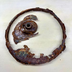 Peut inclure: Un objet métallique rouillé et vieilli, avec un cadre circulaire et un élément central en forme d'œil. Le métal présente des signes de corrosion, avec des nuances de brun, d'orange et des touches de vert. Le design suggère un style vintage ou antique.