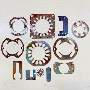 Peut inclure: Ensemble de pièces métalliques de formes irrégulières avec un aspect rouillé et vieilli. Les pièces varient en taille et en forme, avec des formes circulaires et rectangulaires avec des motifs découpés. Les couleurs incluent des nuances de marron, de bleu et de vert.