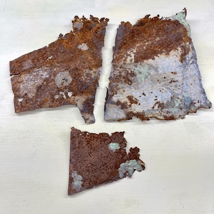 May include: Three irregularly shaped pieces of rusted metal with a textured surface. The metal is primarily brown with areas of blue-green and white. The pieces appear to be torn or broken.
