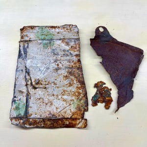 Peut inclure: Plusieurs morceaux de métal rouillé et vieilli. Le plus grand est de forme rectangulaire avec des bords pliés, affichant des teintes de blanc, de gris et de vert. D'autres fragments incluent une pièce façonnée et une petite pièce irrégulière, toutes d'aspect usé.