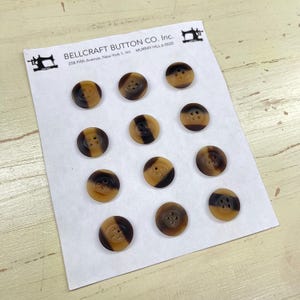 Puede incluir: Una taza de cerámica blanca con un asa negra y el texto "But First, Coffee" en un estilo manuscrito. La taza está sobre una superficie blanca. La taza mide aproximadamente 10 cm de alto.