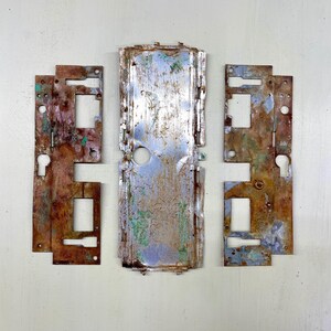 Peut inclure: Ensemble de pièces de quincaillerie de porte en métal vieilli. Les pièces, dont des plaques et un panneau central, présentent un mélange de rouille, de bleu, de vert et de brun, suggérant l'âge et l'exposition. La quincaillerie comporte des trous de serrure et des découpes rectangulaires.