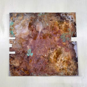 Peut inclure: Une plaque métallique carrée et patinée avec une surface mouchetée. La plaque présente un mélange de couleurs marron, cuivré et turquoise, avec des sections découpées sur les bords. L'effet général suggère une esthétique industrielle ou vintage.