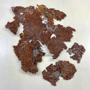 May include: Several irregularly shaped pieces of rusted metal with holes and a rough texture. The metal is primarily shades of brown and orange, with some areas of gray and blue. The pieces are scattered on a white surface.