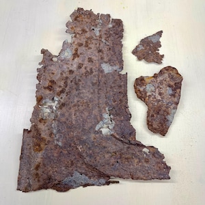 May include: Close-up of several pieces of rusted metal with a textured surface. The metal is primarily brown with areas of gray and white, showing signs of corrosion and age. The pieces are irregularly shaped.