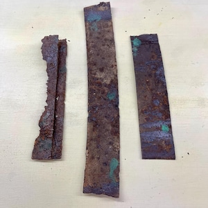May include: Three weathered, rectangular metal pieces with a rusty brown color and patches of green and blue oxidation. The edges are rough and uneven, suggesting age and exposure to the elements. The pieces vary in size and shape.