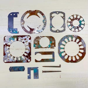 May include: A collection of various metal cutouts with a distressed, aged appearance. The shapes include circles, squares, and irregular forms, with colors of rust, blue, and green. The pieces appear to be components or decorative elements.